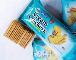 Close-up of blue-packaged cream crackers with several rectangular crackers laid on a white surface.