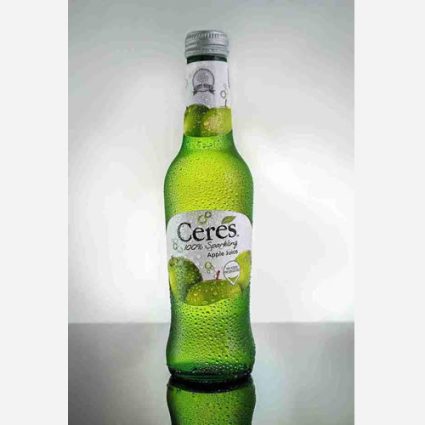 Green glass bottle of Ceres Apple Juice with condensation, standing on a reflective surface.