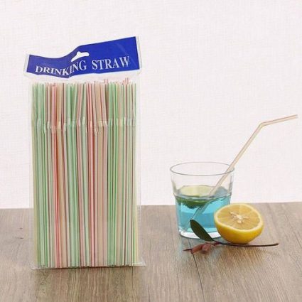 Pack of multi-colored drinking straws beside a glass of blue drink, lemon half, and a light pink straw on a wooden table.