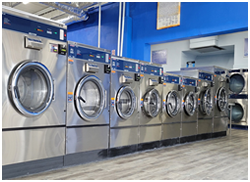 Row of industrial front-loading washing machines in a laundromat with blue walls and a clean, tiled floor