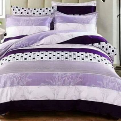 Bed dressed with a purple, lavender, and white comforter set featuring a floral pattern and black-and-white checkerboard borders, with matching pillows.