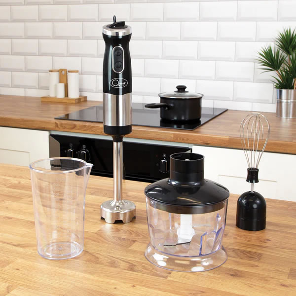 Quest 3-in-1 Stick Blender 700W - Black 5 - Imavug Immersion blender standing upright on a wooden kitchen counter with a blending jar and whisk nearby.