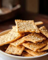 Golden sesame crackers stacked in a white bowl.