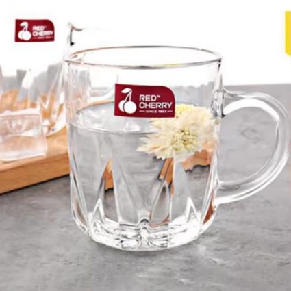 Clear glass mug with a red 'Red Cherry' logo sticker, filled with water, on a grey countertop.
