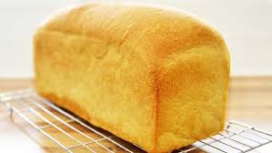 Golden loaf of bread cooling on a metal wire rack in a kitchen window light.