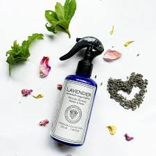 Blue spray bottle labeled Lavender calming mist on a white background, surrounded by green leaves and flower petals.