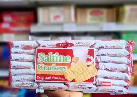 Stack of saltine cracker packages, with a front wrapper showing the label 'Saltine Crackers' and an image of crackers in the center.