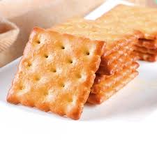 Stack of square salted crackers on a white plate on a light surface