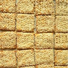 Close-up of sesame-covered brittle squares arranged in a grid on a light surface.