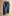 Pair of dark blue jeans with multiple fabric patches and distressed areas, laid flat on a wooden floor; cuffs rolled to show plaid lining.
